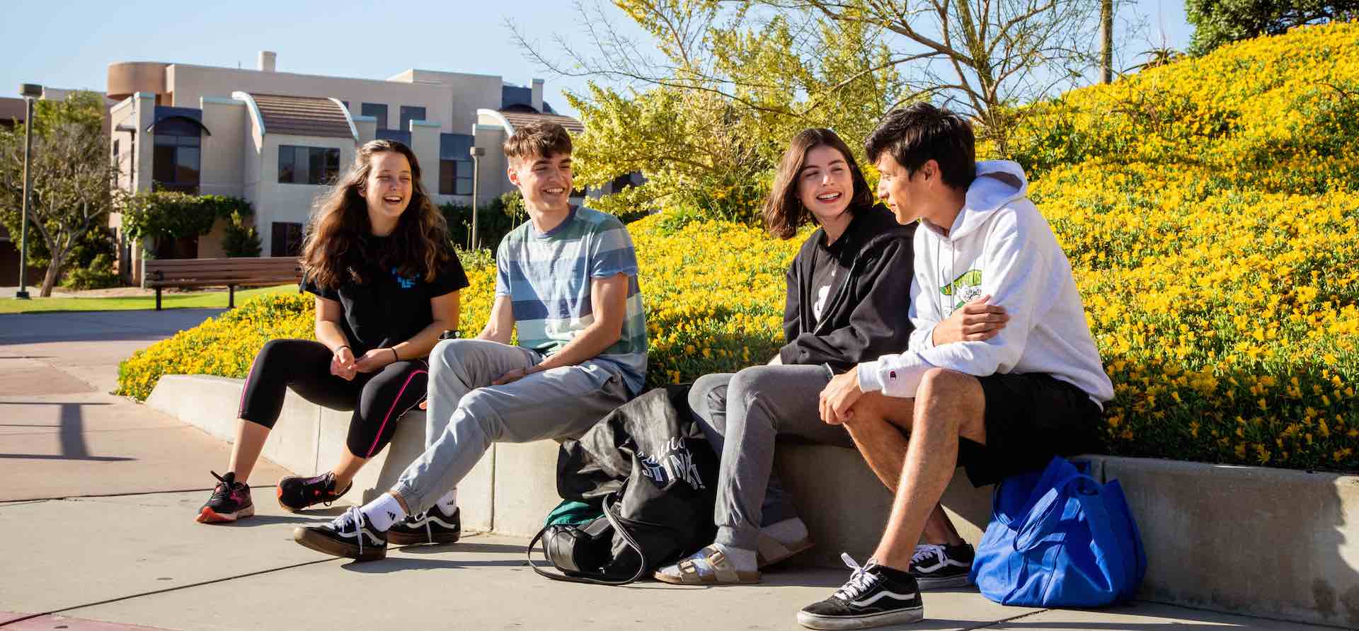four students sitting outdoors smiling and interacting